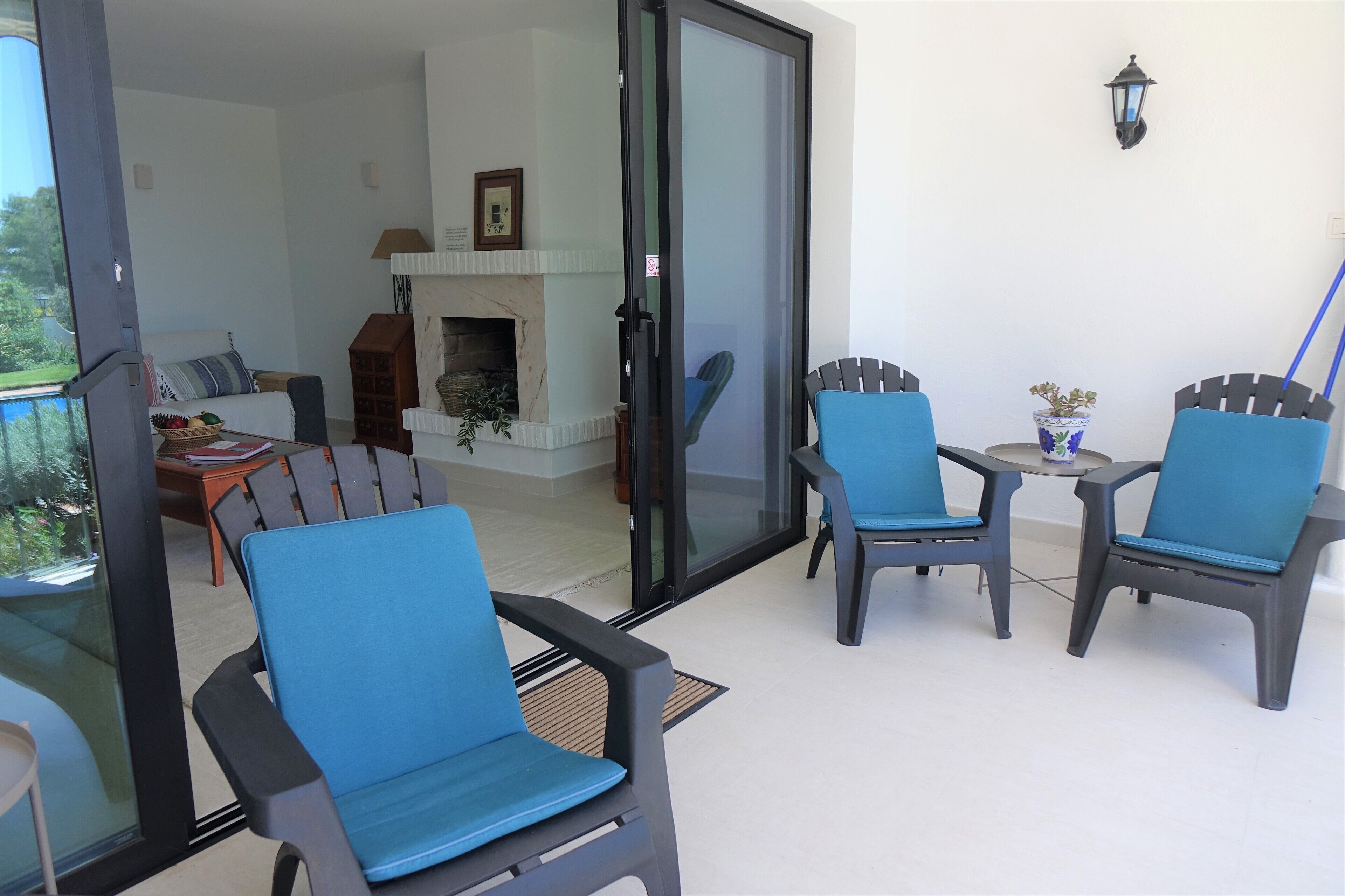Un espace patio doté d’une porte vitrée donnant sur un salon, aménagé avec un canapé, une petite table et des chaises.
