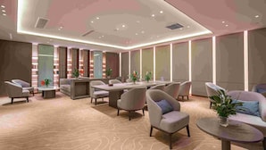Een moderne hotellobby met een centrale zithoek, een receptiebalie en een boekenkast.