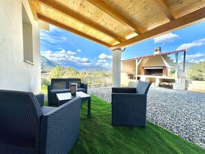 Eine Terrassengartenanlage mit Korbmöbeln, einem Grill und Blick auf Berge.