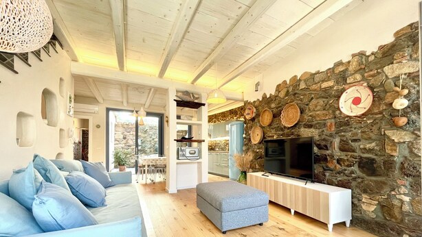 A modern living room with a stone wall, a flat-screen TV, a sofa, and a dining area.