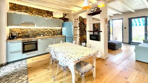 A modern kitchen with a stone backsplash, wooden ceiling, and a dining area with a patterned tablecloth.