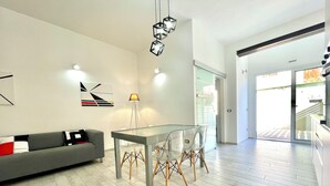 A modern living room with a grey sofa, a glass dining table with chairs, and a pendant light.