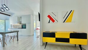 A modern kitchen with white cabinetry, a dining area with a glass table, and a yellow and black console table.