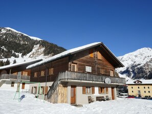 Un chalet en bois doté d’un balcon, entouré de montagnes enneigées.