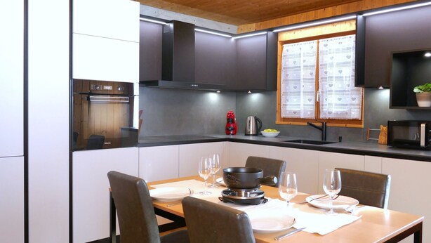 Cozinha moderna com armários escuros, teto de madeira e área de jantar com mesa posta para quatro pessoas.