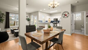 A spacious living area with a wooden dining table, grey chairs, and a chandelier. - Cozy Retreat With Arcade Haven (Austin)