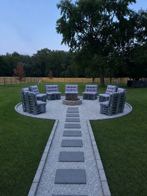 Un aménagement circulaire avec six chaises disposées autour d’un foyer central, le tout étant entouré d’un chemin de gravier.