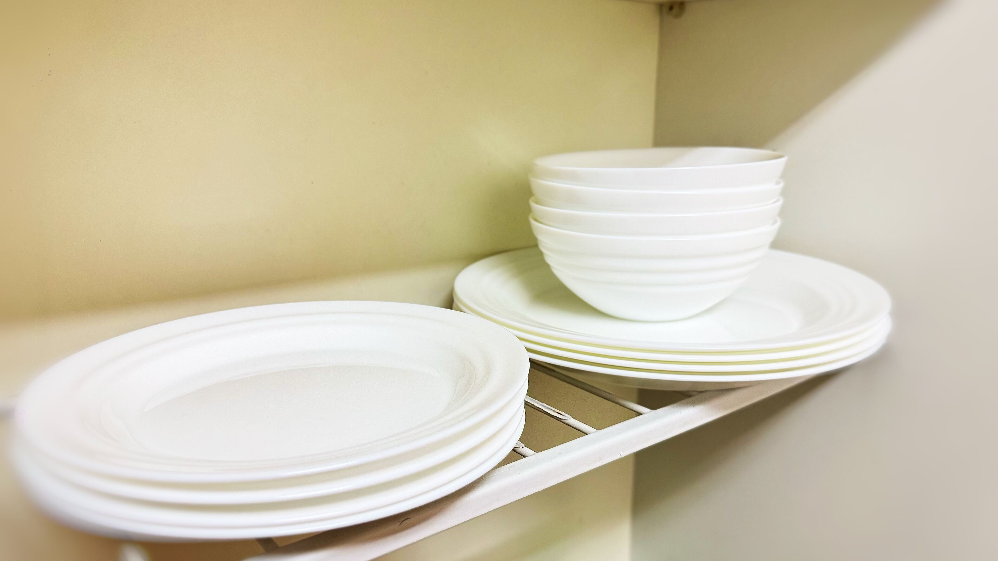 A set of white plates and bowls stacked on a metal rack in a kitchen.