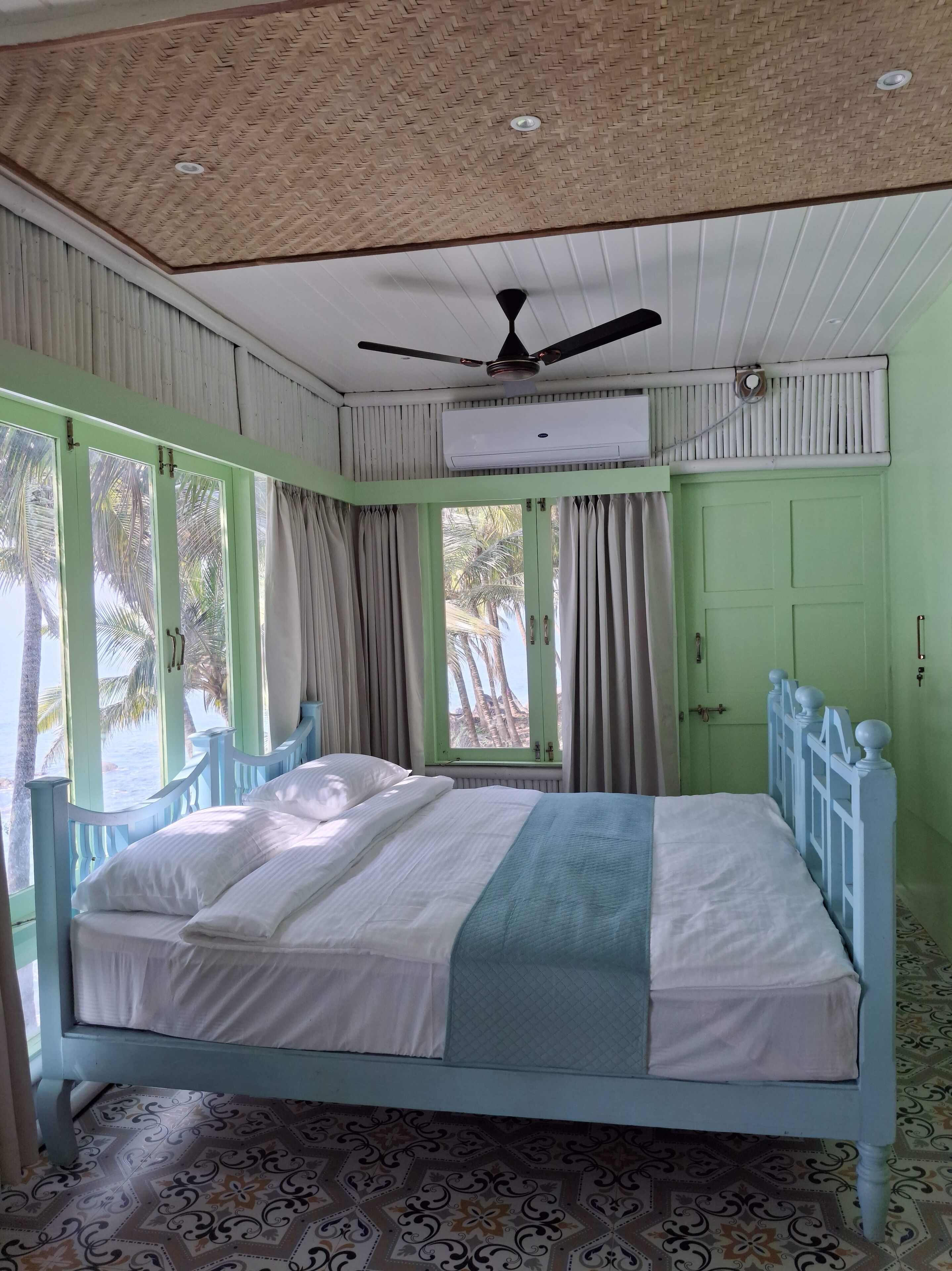 A room with a bed, a ceiling fan, an air conditioning unit, and a window with curtains.