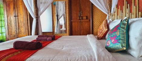A bed with white linens, a red blanket, and a red towel. There are two pillows with colorful patterns. The room has wooden furniture and a canopy bed.