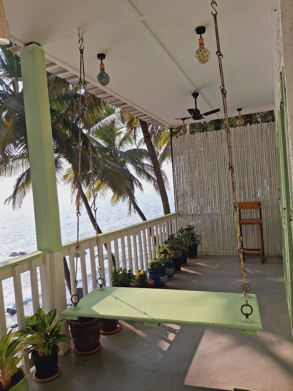 Un espacio al aire libre cubierto con una hamaca, plantas en macetas y vistas a palmeras y al mar.