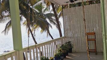 Un espacio al aire libre cubierto con una hamaca, plantas en macetas y vistas a palmeras y al mar.