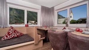 Quarto moderno com um banco de madeira, mesa de jantar com cadeiras e amplas janelas com vista para as montanhas.