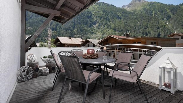 Um deck de madeira com uma mesa redonda e cadeiras, com vista para uma paisagem montanhosa.
