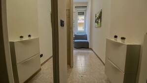 Un couloir étroit, avec une porte au fond qui donne sur une pièce contenant un lit et une fenêtre.
