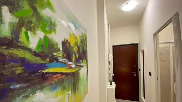 Un couloir orné d’un grand tableau abstrait au mur, un comptoir d’accueil blanc et une porte au fond.
