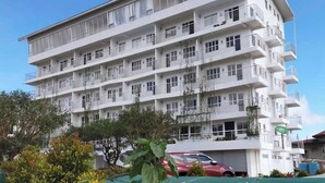 Un hotel de varios pisos con balcones, zona de estacionamiento y jardín con flores rojas.
