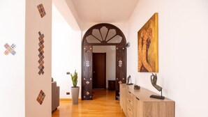 Un pasillo con suelo de madera, un arco decorativo, una planta en maceta y un armario de madera con una escultura.