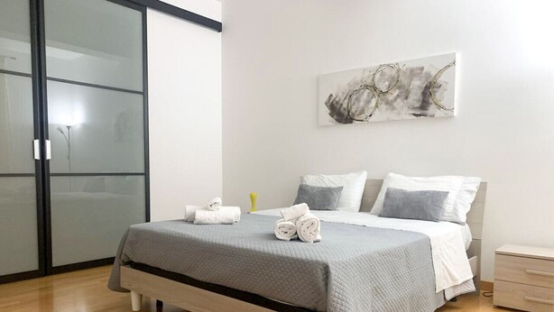 Un dormitorio moderno con cama, mesita de noche y una obra de arte colgada en la pared.