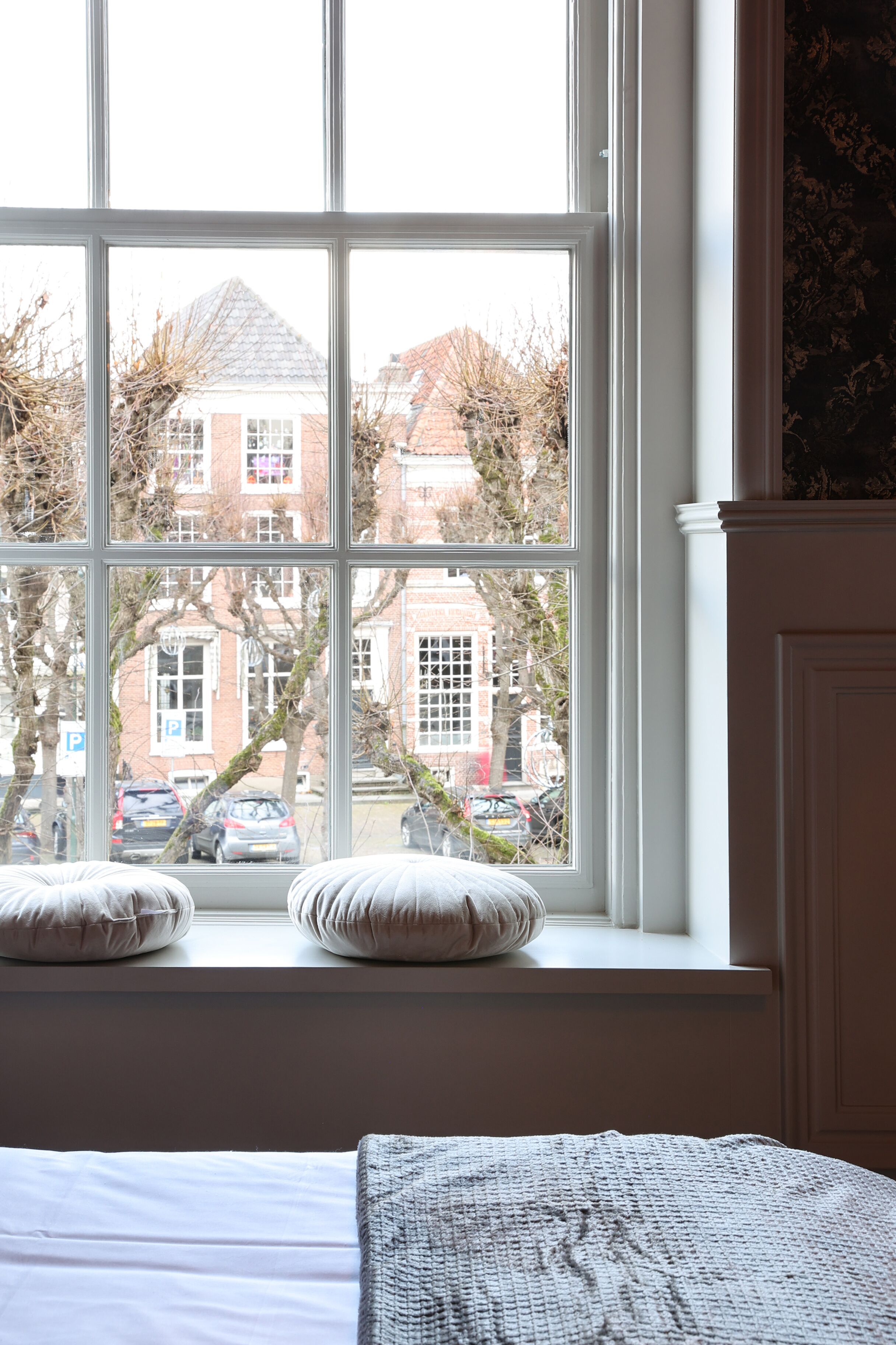 A bedroom with a large window, a bed with white bedding, and two pillows on the windowsill.