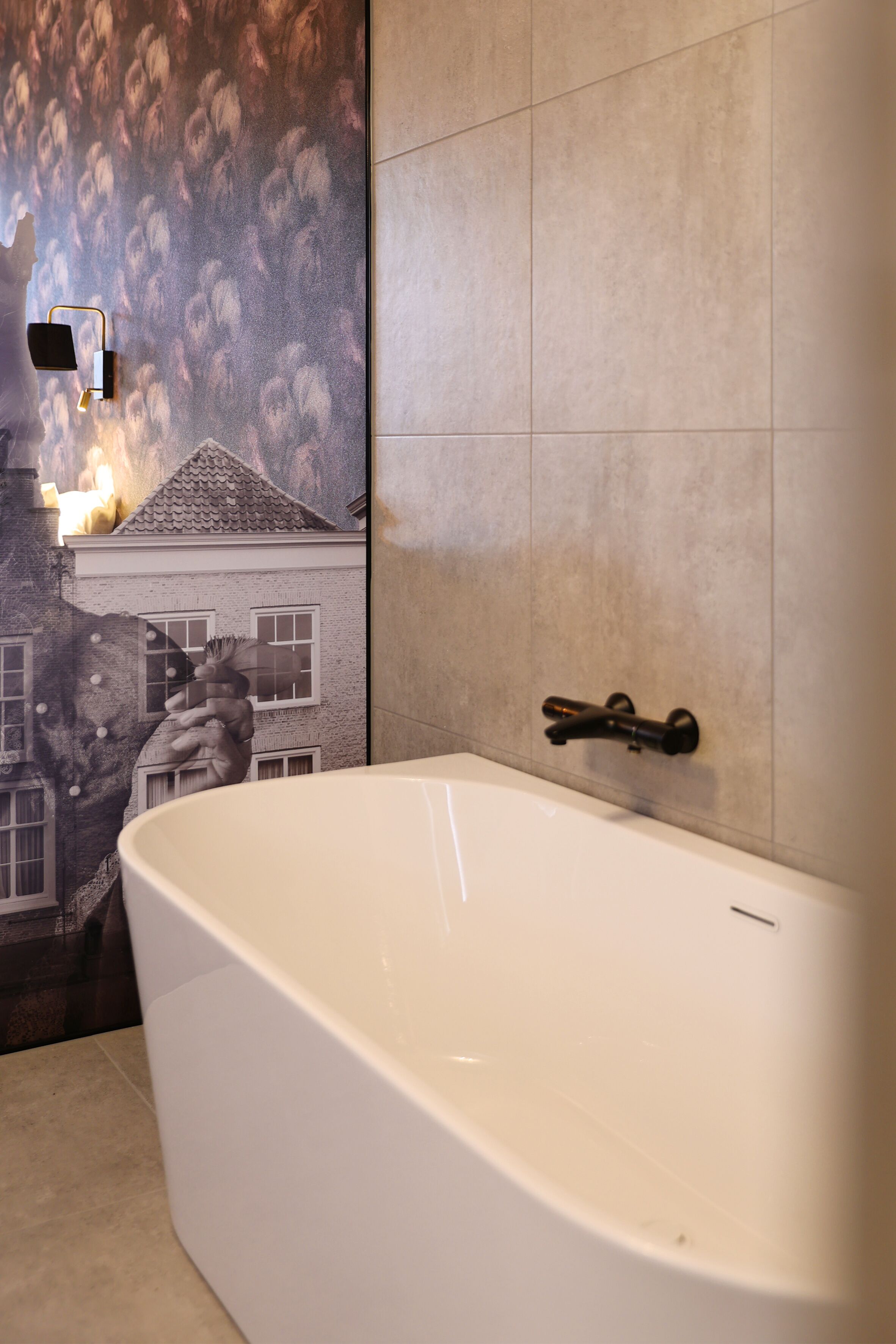 Een moderne badkamer met een groot bad, betegelde muren en een muurschildering van een gebouw.
