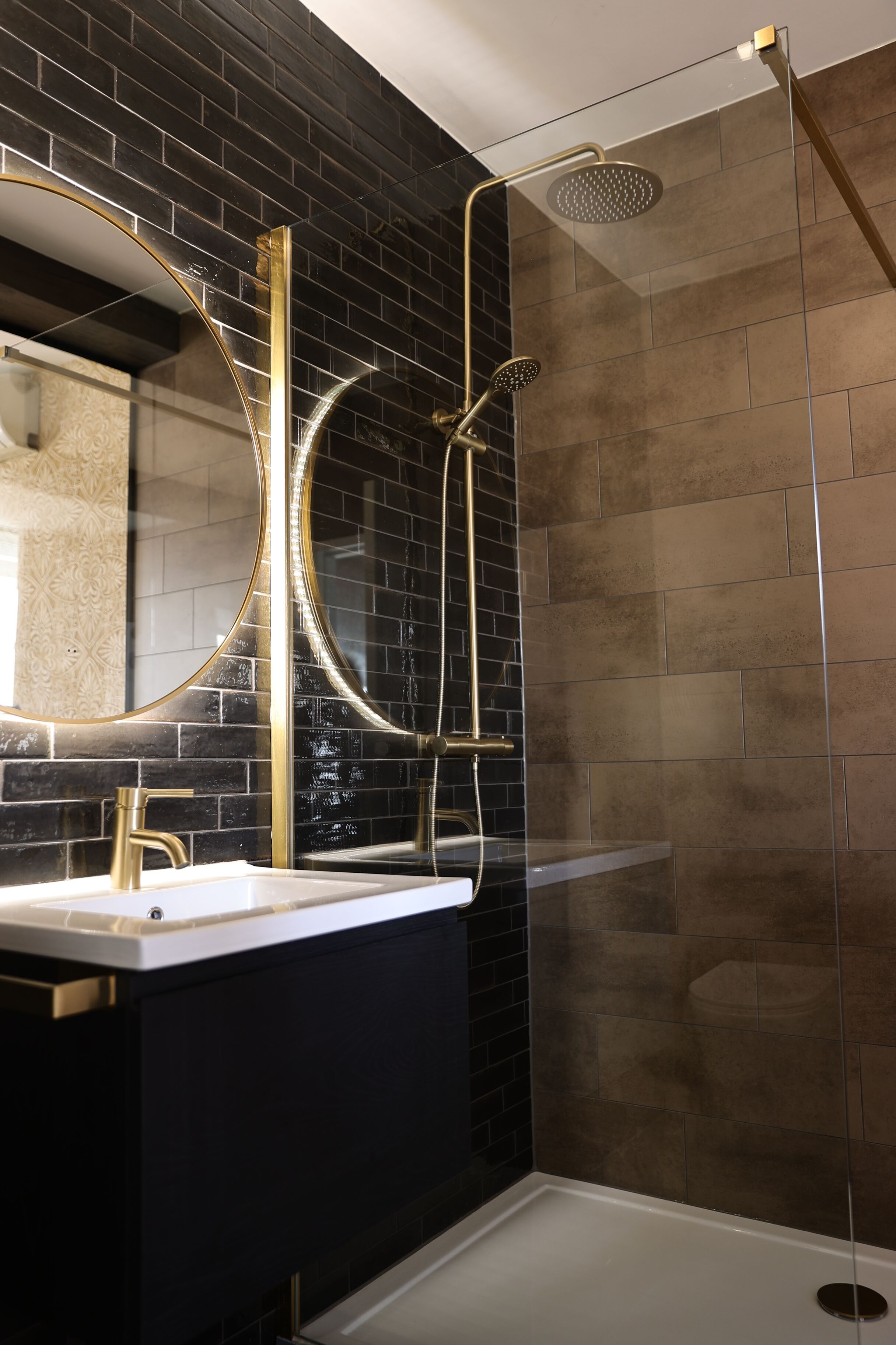Een moderne badkamer met een zwart betegelde muur, een spiegel met gouden lijst, een wit wastafelmeubel en een douchecabine met glazen wanden.
