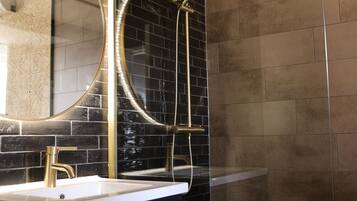 Een moderne badkamer met een zwart betegelde muur, een spiegel met gouden lijst, een wit wastafelmeubel en een douchecabine met glazen wanden.