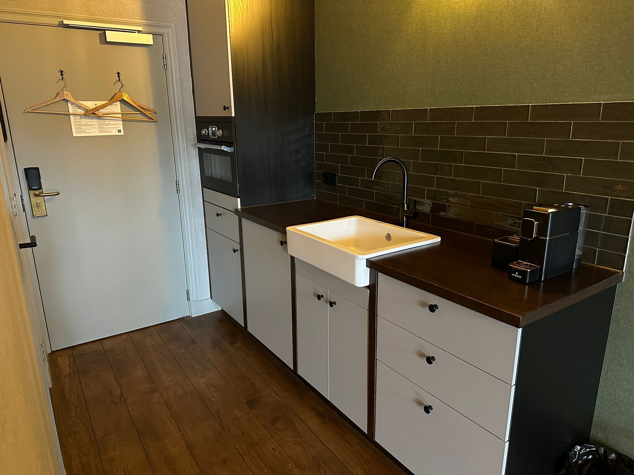 Een kleine keuken met een wit spoelgedeelte, een donker aanrecht en houten vloeren.