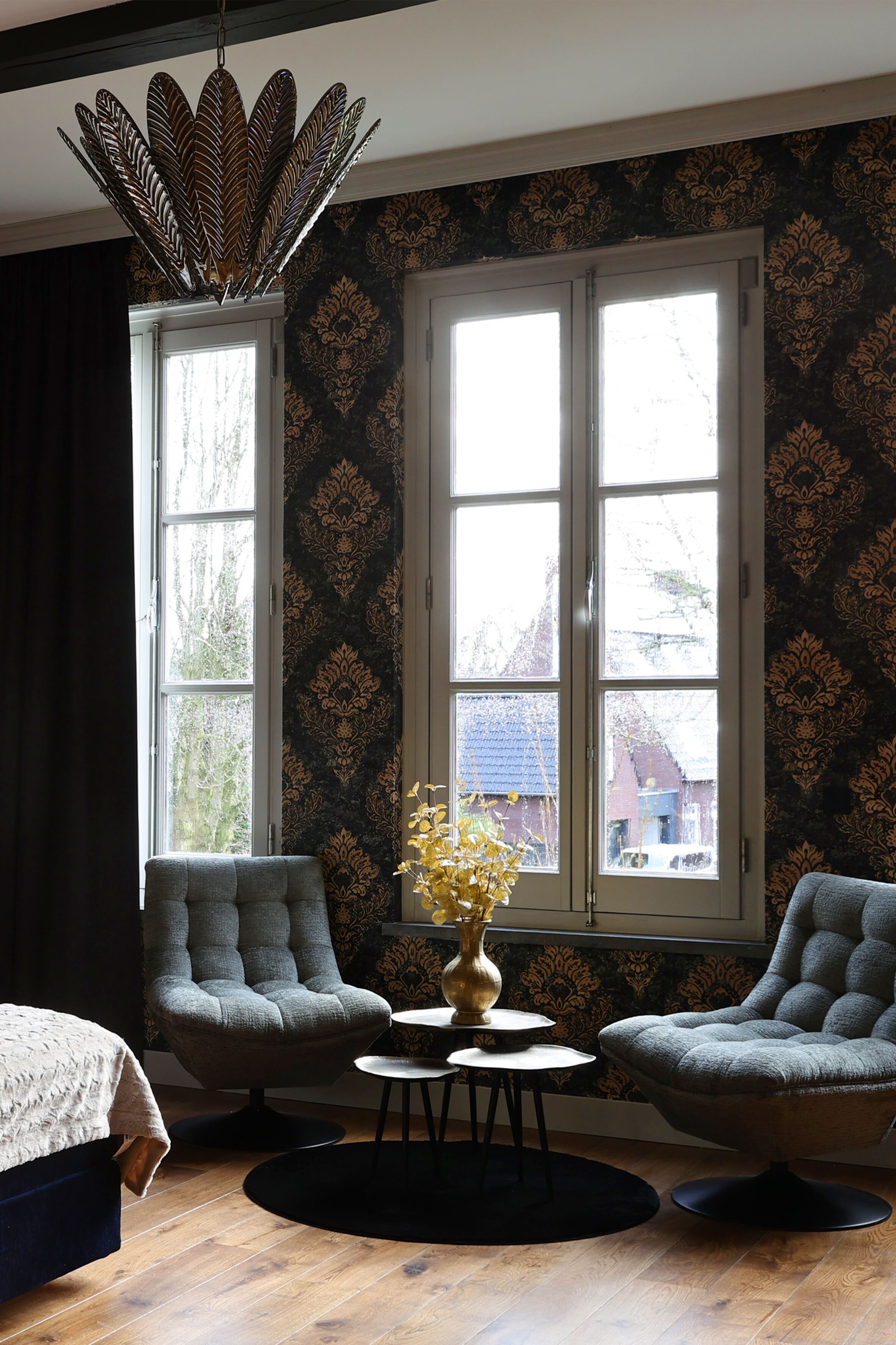 Una habitación con dos sillones, una mesita redonda, un jarrón decorativo y un amplio ventanal con vistas a edificios.