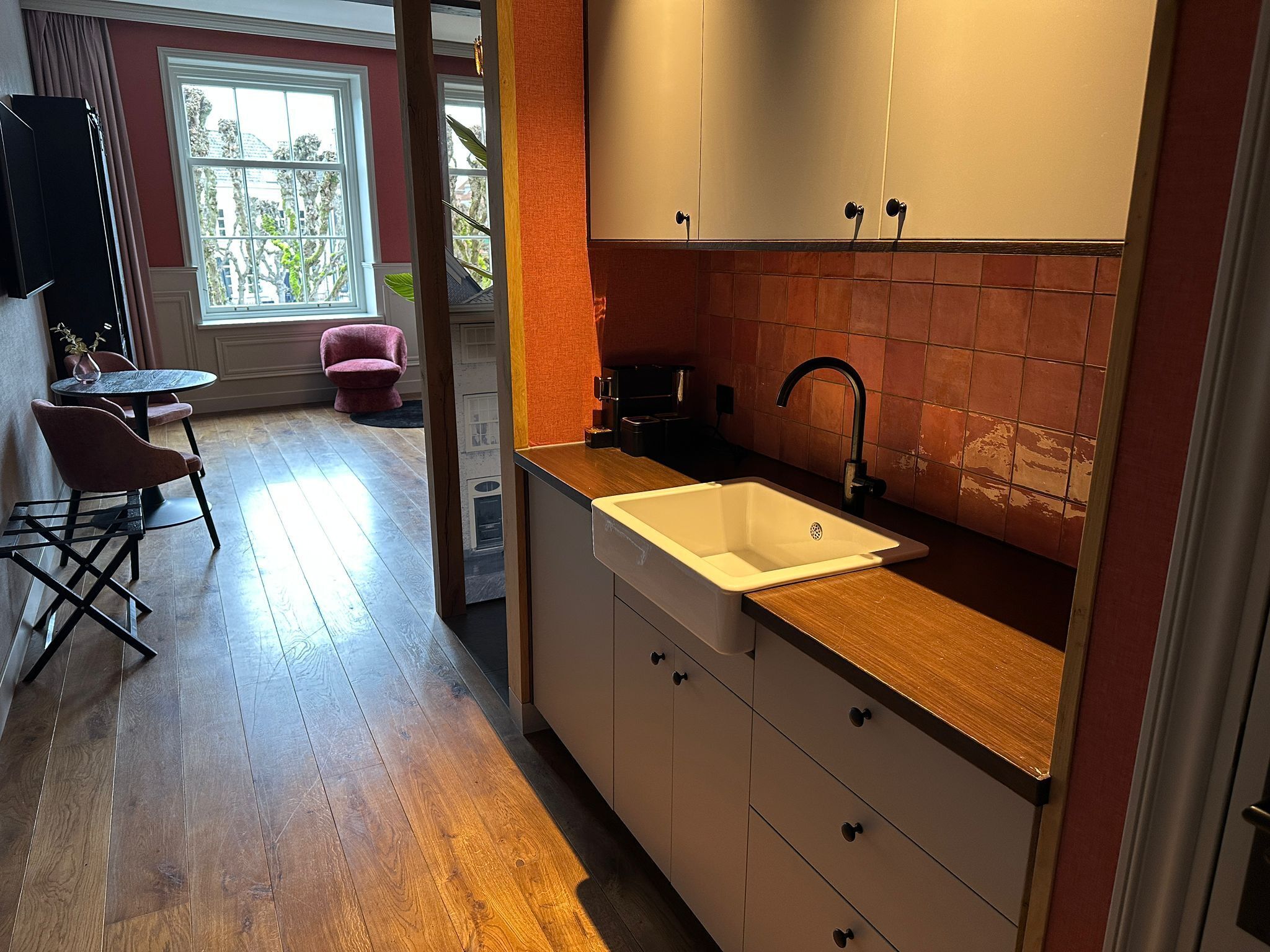 Cocina moderna con un lavamanos blanco, encimera de madera y vistas al exterior a través de una ventana.