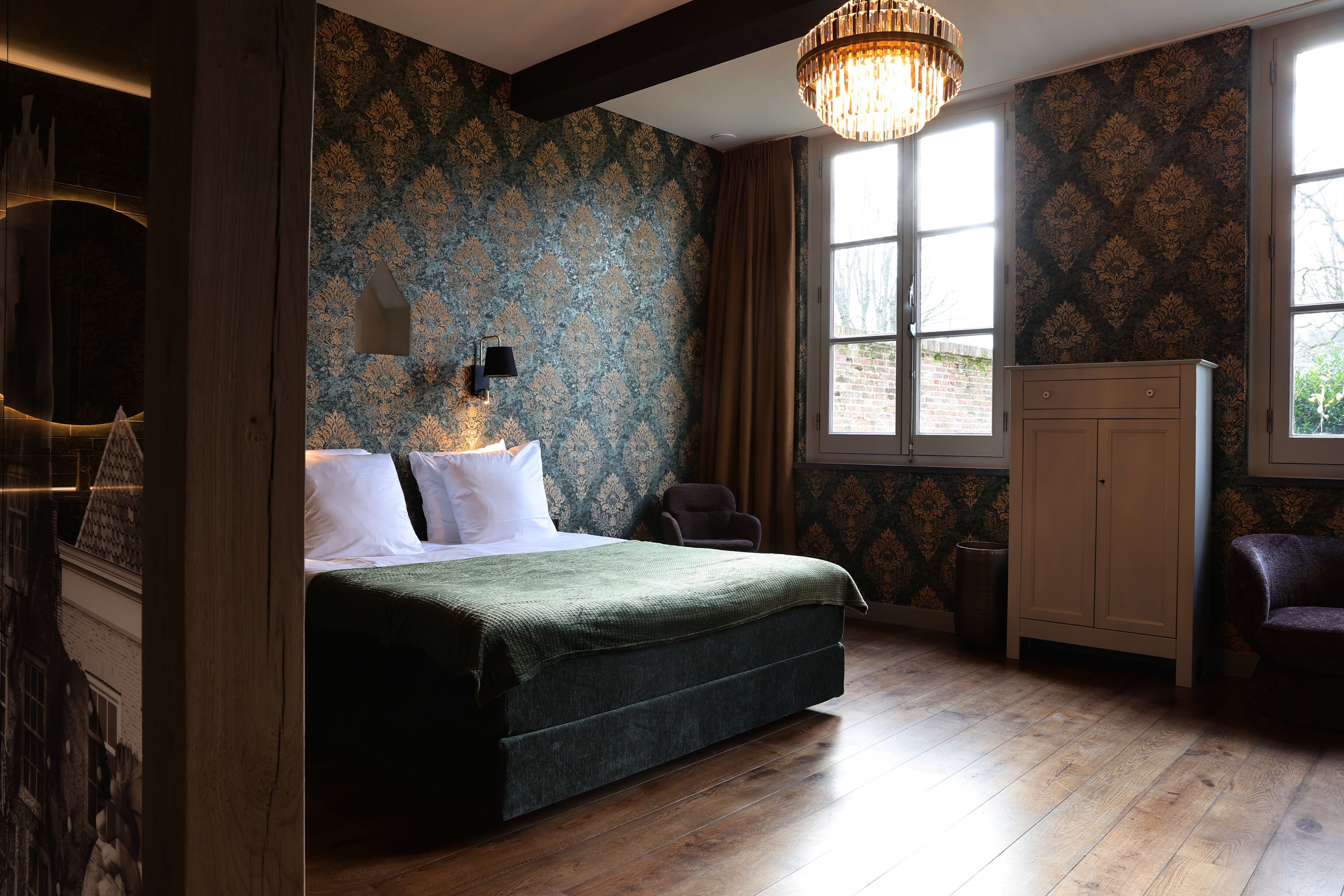 Un dormitorio con una cama grande, un candelabro, un armario y una ventana con cortinas.
