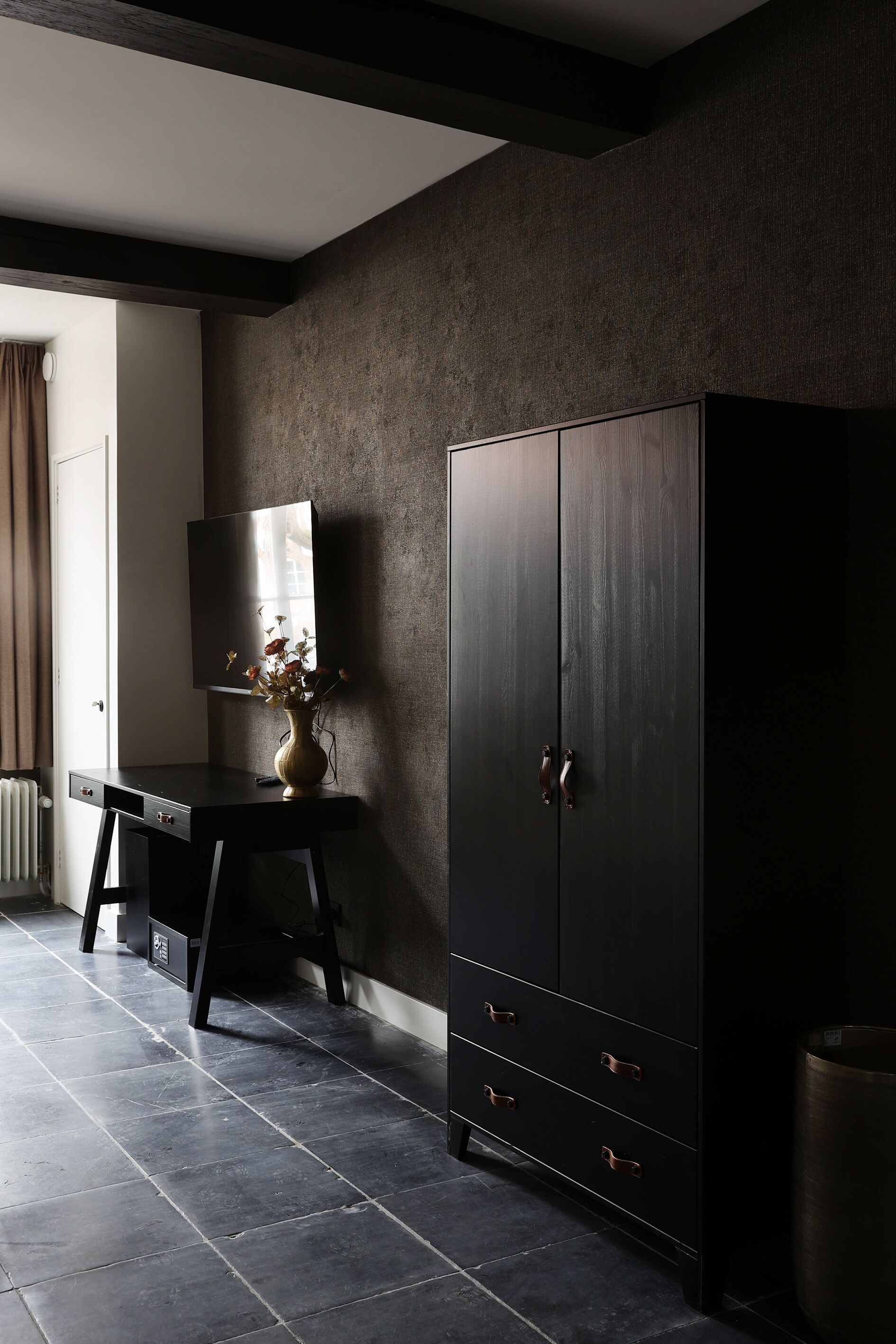 Une pièce avec une armoire en bois foncé, un bureau agrémenté d’un vase et un grand miroir.