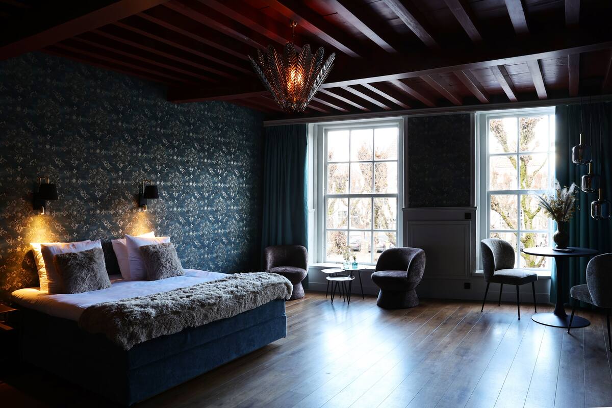 A bedroom with a large bed, two chairs, a small table, and a window with curtains.