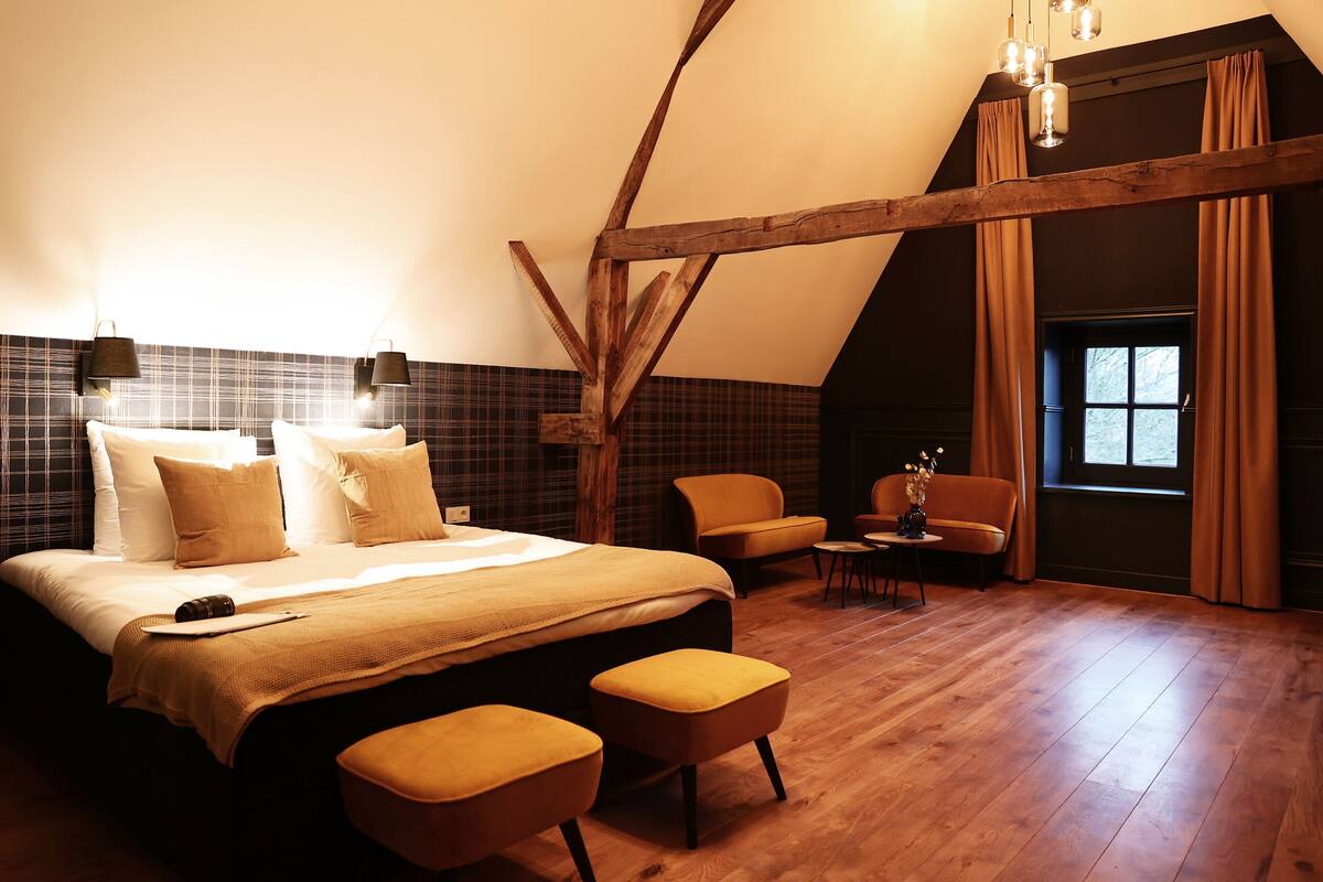A bedroom with a large bed, two bedside tables, a chair, and a small table with a vase.