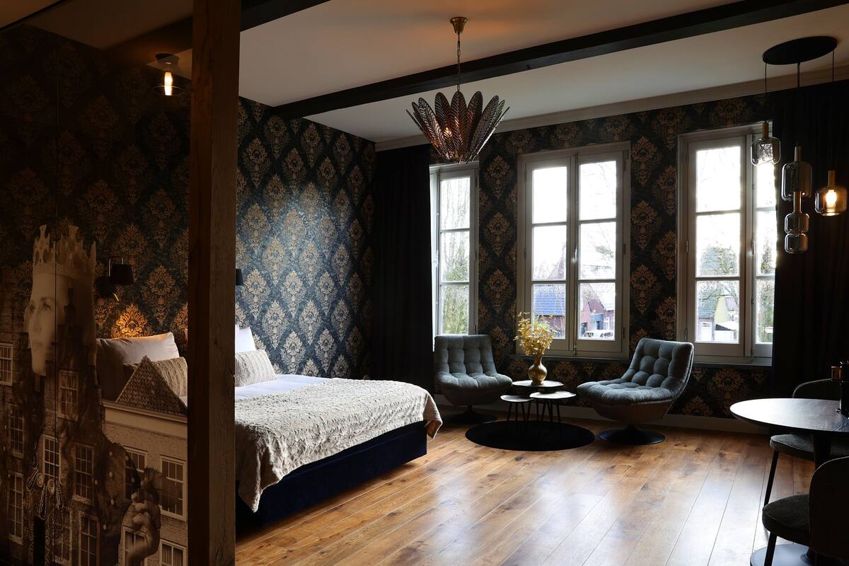A bedroom with a large bed, two armchairs, a round table, and a window with a view.