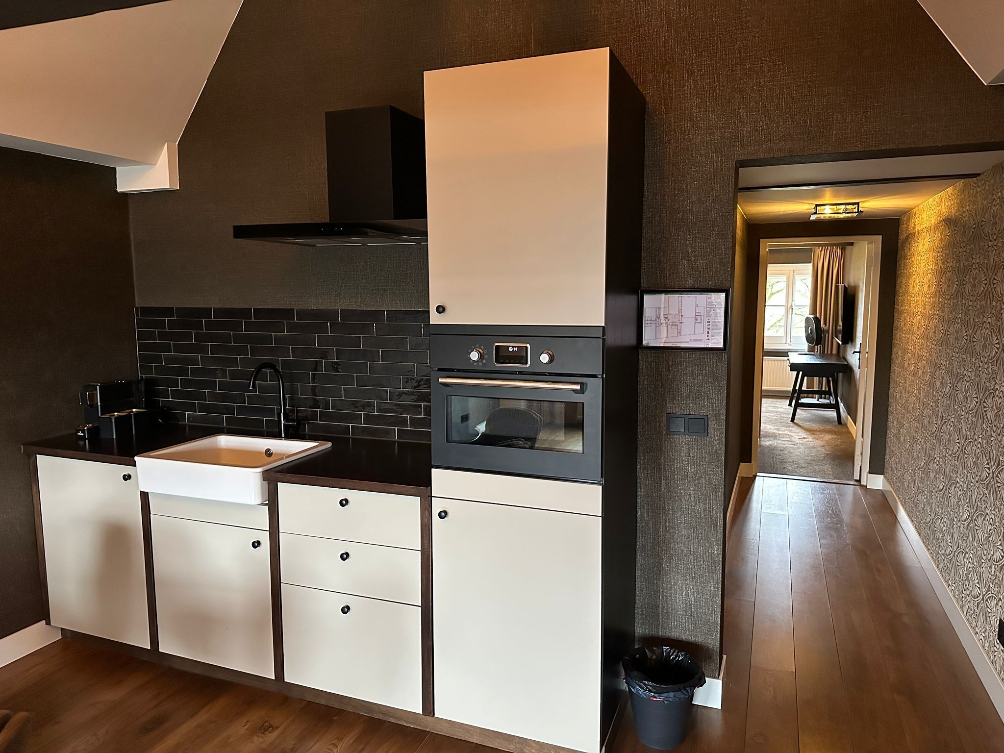 Una cocina moderna con salpicadero de azulejos negros, armarios blancos y horno empotrado.