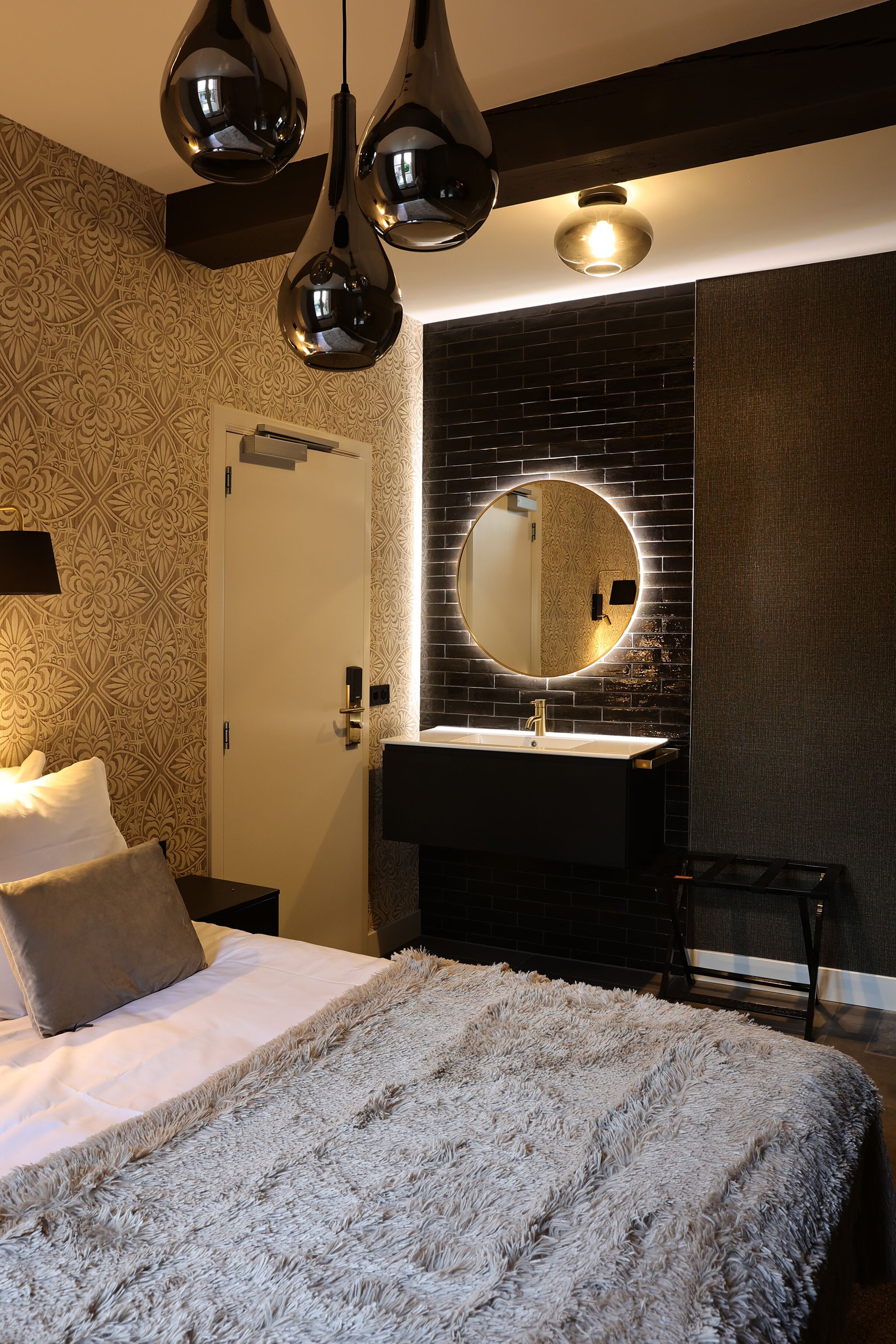 Un dormitorio con cama, un espejo redondo, un lavabo negro y papel tapiz estampado.