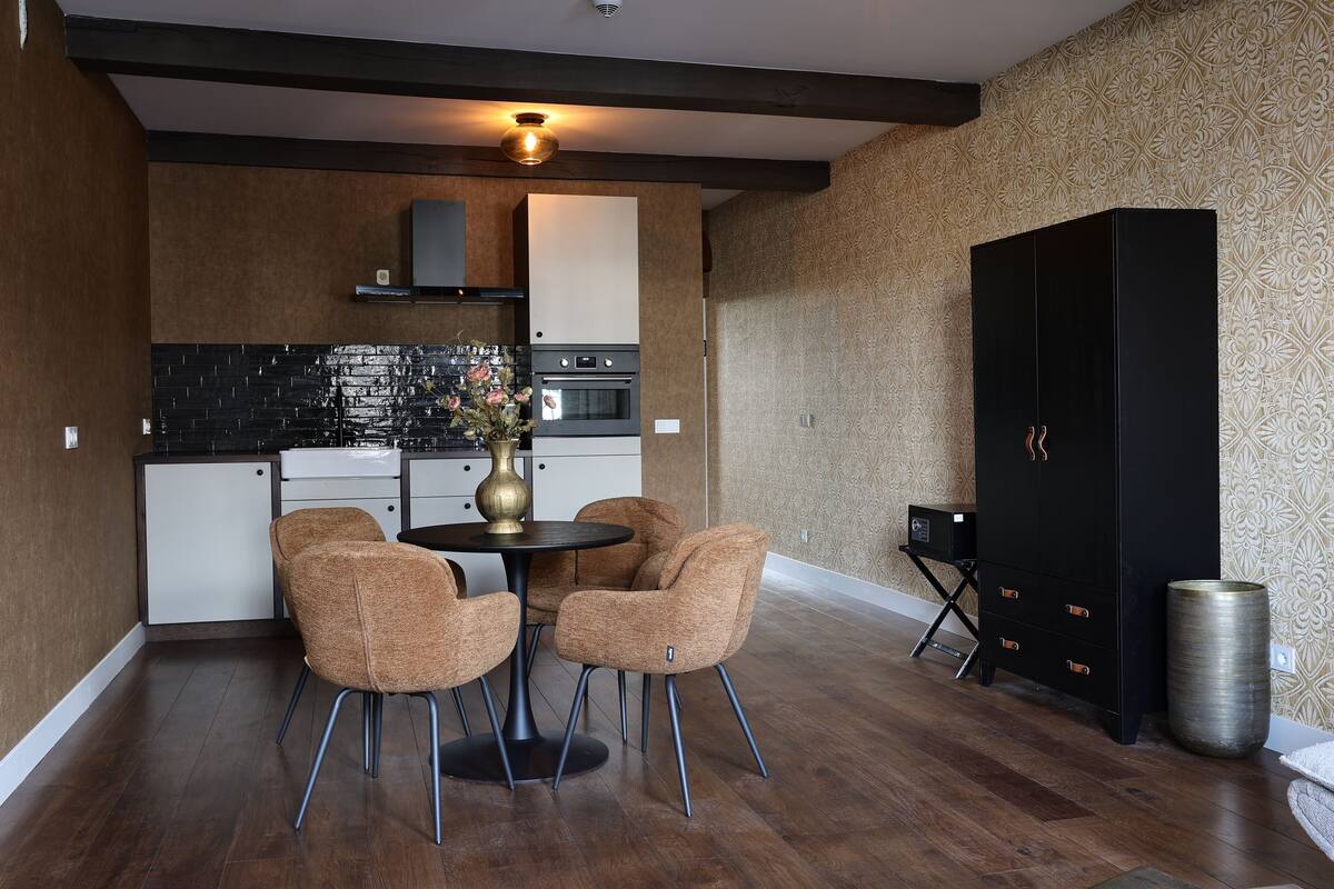 A compact kitchen with modern appliances, a dining area with two chairs, and a black cabinet.