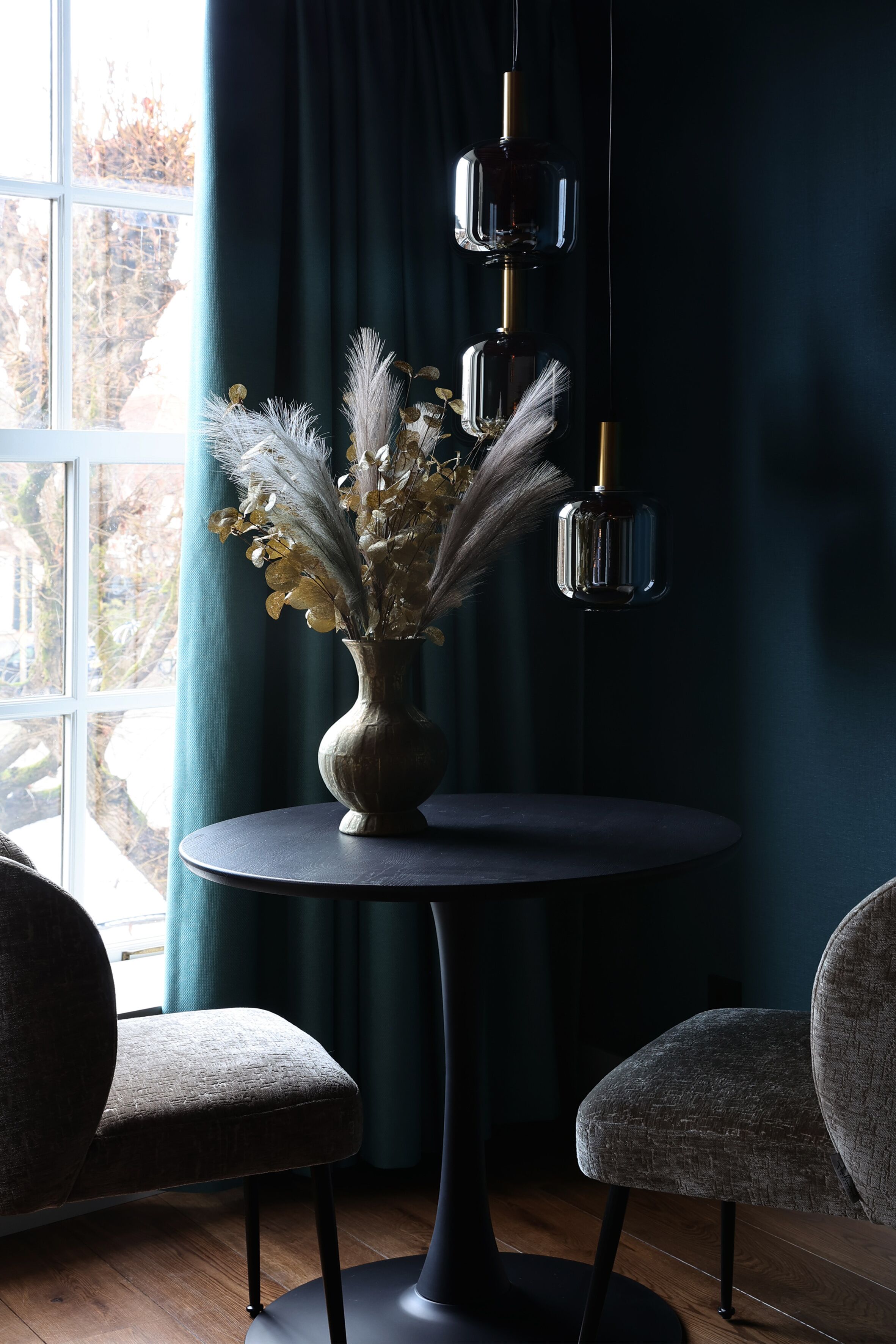 Een kamer met een ronde tafel, twee stoelen, een vaas met gedroogde bloemen en hangende hanglampen.
