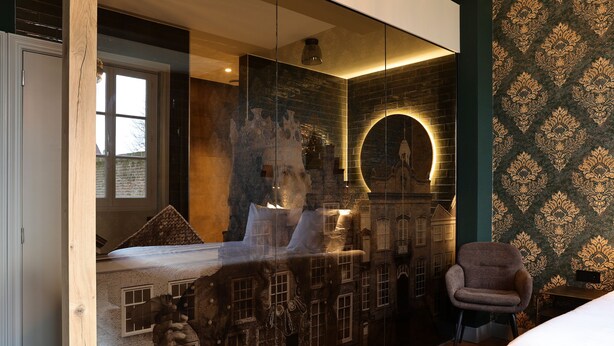A modern bedroom with a large bed, a chair, and a wall with a decorative pattern. - Stadshotel Geertruidenberg (Geertruidenberg)