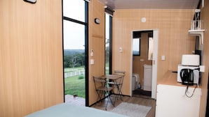 Ein Zimmer mit einem Bett, einem Tisch mit Stühlen, einer Mikrowelle und Blick ins Freie.