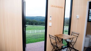 Ein Zimmer mit Holztisch und -stühlen, Blick auf ein grünes Feld und einen weißen Zaun, sowie eine Holztür.