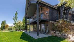 Une maison moderne à deux étages dotée d’un patio couvert, d’un espace salon extérieur et d’un mur de soutènement en pierre.