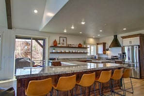 Une cuisine moderne dotée d’un grand îlot central, de tabourets de bar, d’appareils électroménagers en acier inoxydable et d’armoires en bois.