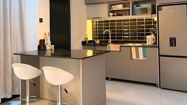 A modern kitchen with a central island, two bar stools, a microwave, and a refrigerator. - Ace Homes Kampala (Kampala)