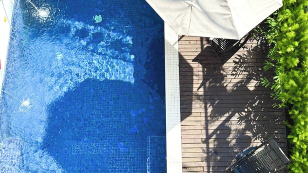Ein Schwimmbecken mit einer befliessten Kante, einer Holzterrasse und einem weißen Sonnenschirm.