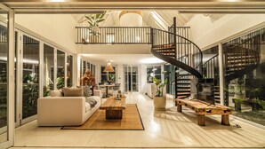 Un vaste espace de vie agrémenté d’un escalier moderne, de grandes fenêtres et d’un coin salon confortable.
