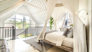Une chambre à coucher avec un lit à baldaquin, une vue sur la verdure et un balcon doté d’une balustrade.