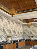 A modern hotel lobby with marble walls, wooden reception desk, and gold chandeliers.