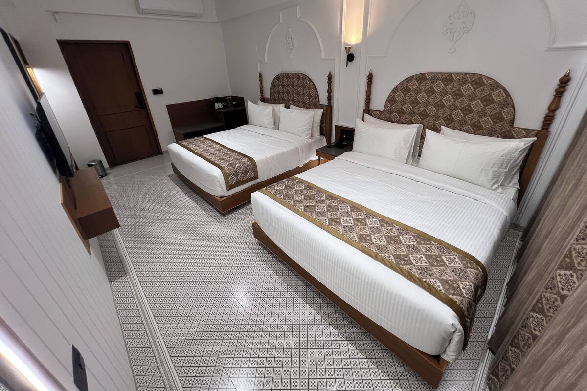 Quarto de hotel com duas camas, um guarda-roupa, uma escrivaninha e um espelho.